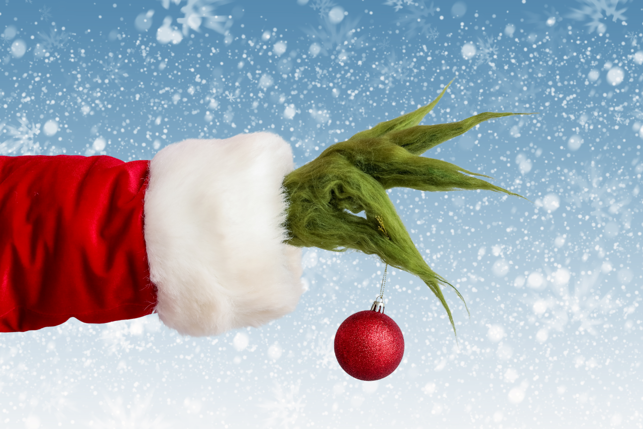 A green hand in a Santa costume holding a red Christmas ornament against a snowy background. Holiday decor, festive season, whimsical Christmas image.