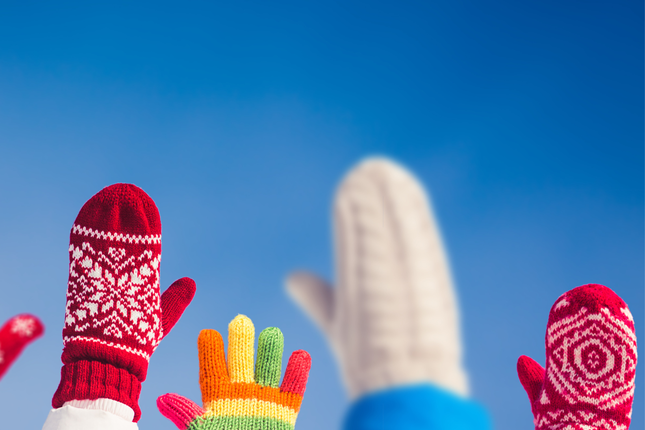 Colorful winter gloves and mittens raised against a clear blue sky, showcasing vibrant designs and warm knitwear ideal for cold weather, winter fashion trends, and holiday season accessories.