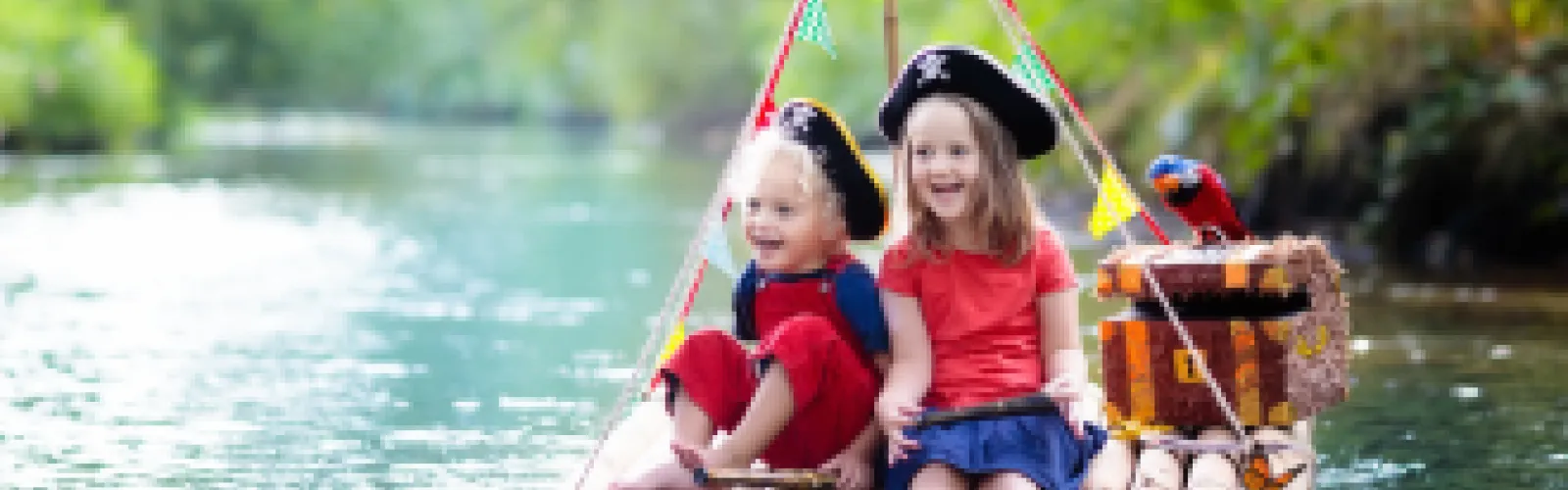 Children wearing pirate hats on a wooden raft floating in a gentle stream