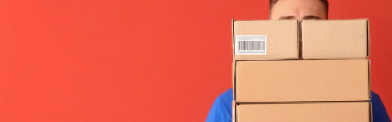 Man in blue t-shirt holding brown boxes that are piled so high they cover his eyes.